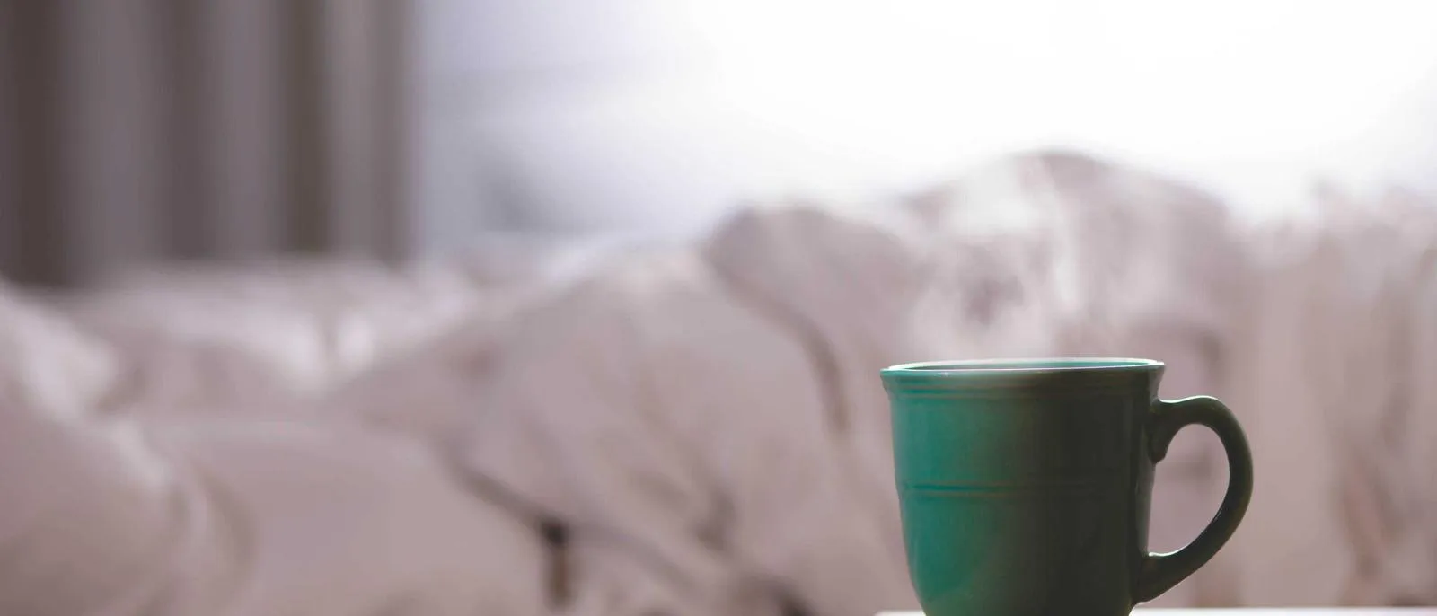 Tasse auf einer weißen Bettdecke im Morgenlicht